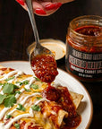 Spoonful of habanero salsa being added to enchiladas with a jar of Sauce Boss Gang Habanero Heatwave salsa.