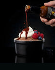 Chocolate sauce being poured over a dessert with berries on a black background