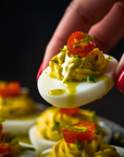 Deviled egg with avocado and cherry tomatoes held by a hand against a dark background