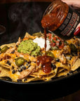 Person pouring sauce over loaded nachos with a blurred background