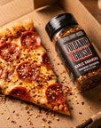 Slice of pizza with pepperoni next to a bottle of Volcanic Crush Garlic Habanero seasoning in a cardboard box.