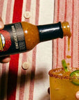 Hand pouring hot sauce into a margarita with a red and white striped shirt in the background