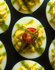 Deviled eggs with green verde salsa and cherry tomatoes on a black surface