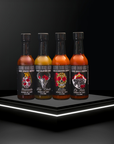 Four bottles of hot sauce with colorful labels on a black platform with white lighting.