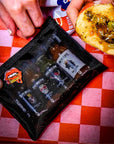 Sauce Boss Gang travel size hot sauce travel pouch on a table with a sandwich.