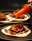 Sauce Boss Gang garlic habanero hot sauce pouring over short rib tacos.