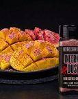 Sauce bottle labeled 'Inferno Dust' next to a plate of sliced yellow and red fruit on a dark background