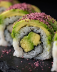 Sushi roll with avocado and pink toppings on a dark surface