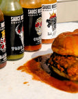 Sauce Boss Gang "The Whole Gang" hot sauce collection dripping on saucy chicken sandwich.