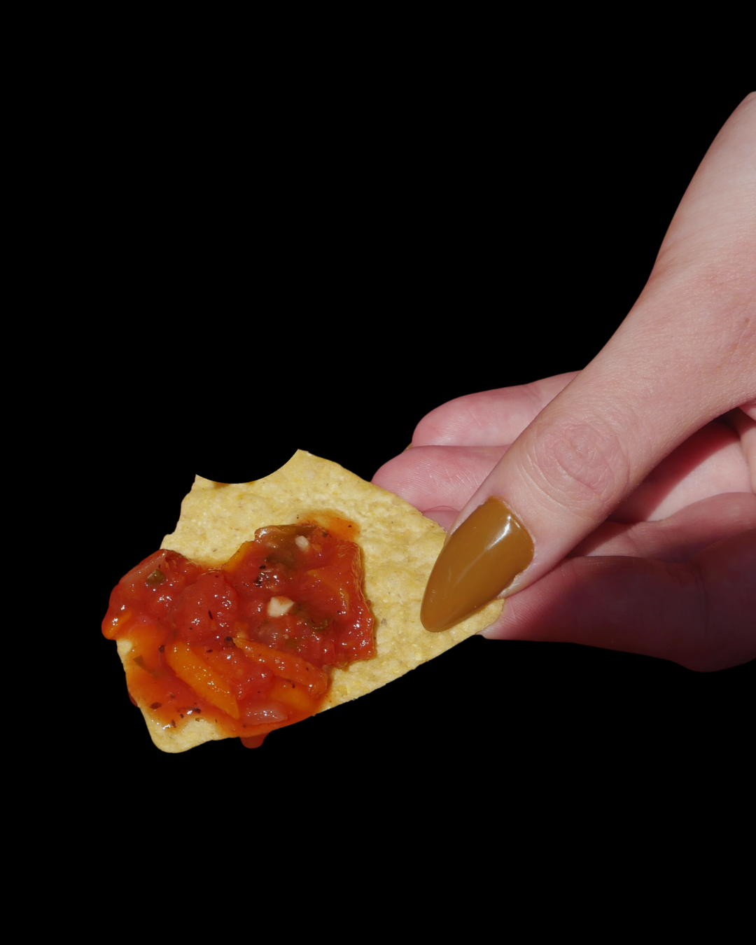 Hand holding a tortilla chip with salsa on a black background