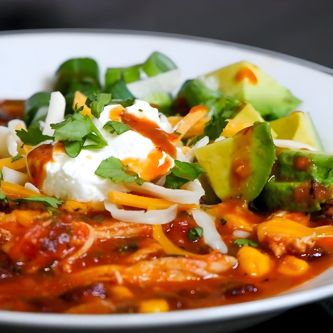  bowl of chili with avocado, sour cream, and cheese on a white plate