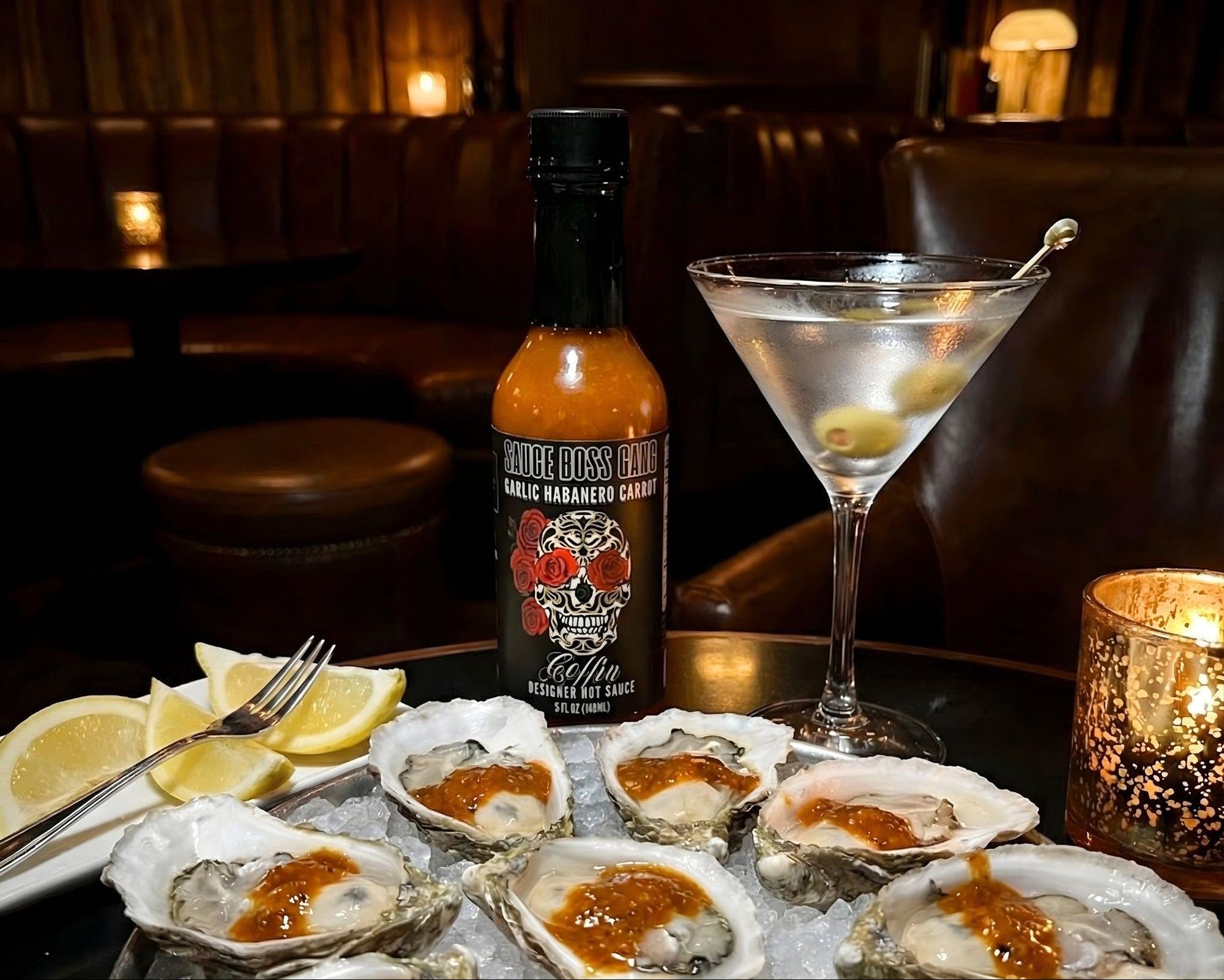Oysters on a half shell with a bottle of hot sauce and a cocktail in a dimly lit bar.