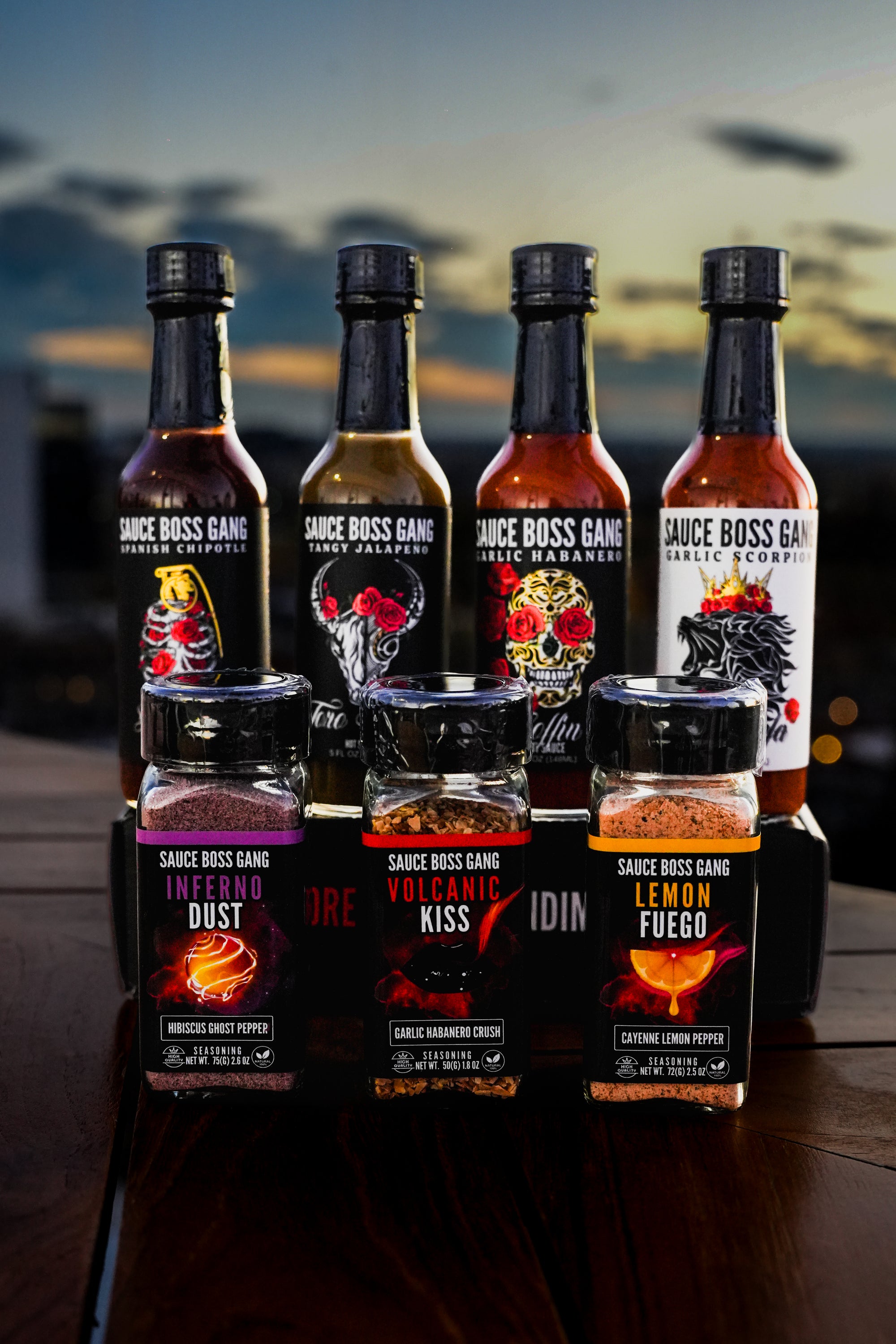 The whole gang hot sauce collection and the viva la noche seasoning collection front view at a restaurant at sunset.