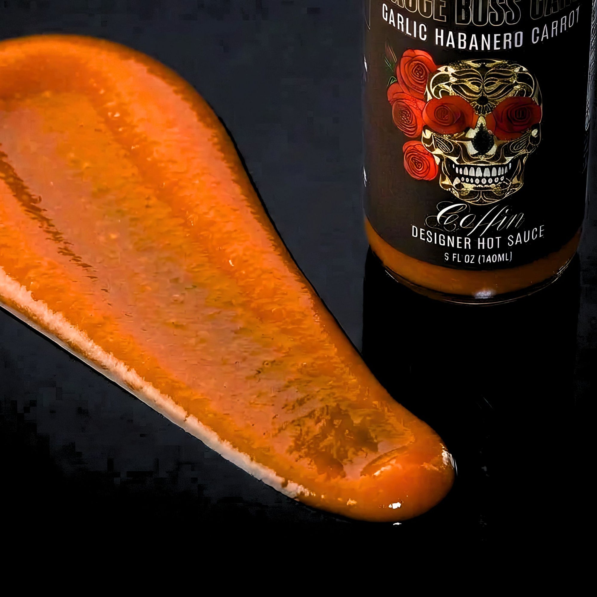Hot sauce bottle with a skull design next to a spread of hot sauce on a dark surface