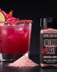 Margarita with lime and flower garnish next to a bottle of 'Inferno Dust' seasoning.