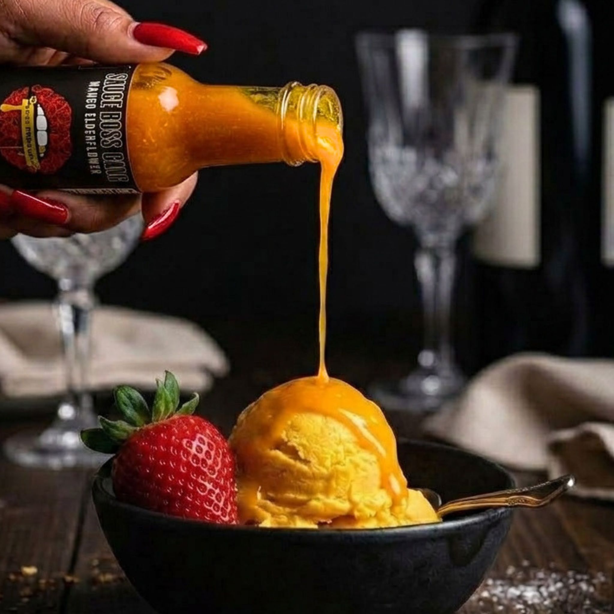 Hot sauce being poured onto a scoop of ice cream with a strawberry on a table setting.