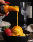 Hot sauce being poured onto a scoop of ice cream with a strawberry on a table setting.