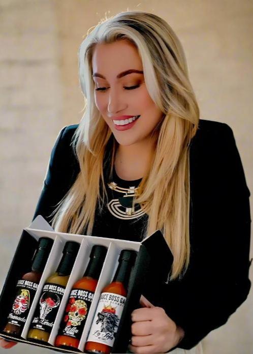 Nicole DiTommaso, owner of Sauce Boss Gang hot sauce, holding The Whole Gang hot sauce collection.