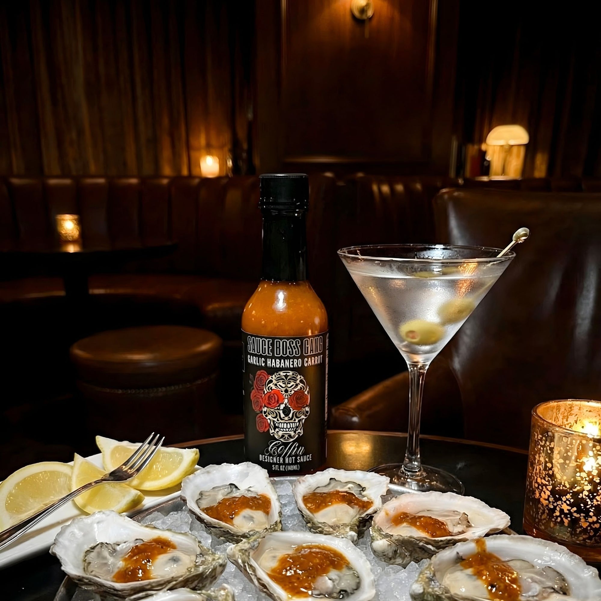 Oysters on a half shell with a bottle of hot sauce and a cocktail in a dimly lit bar.