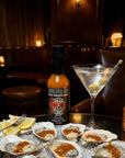 Oysters on a half shell with a bottle of hot sauce and a cocktail in a dimly lit bar.