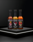 Three bottles of hot sauce on a black platform with a dark background