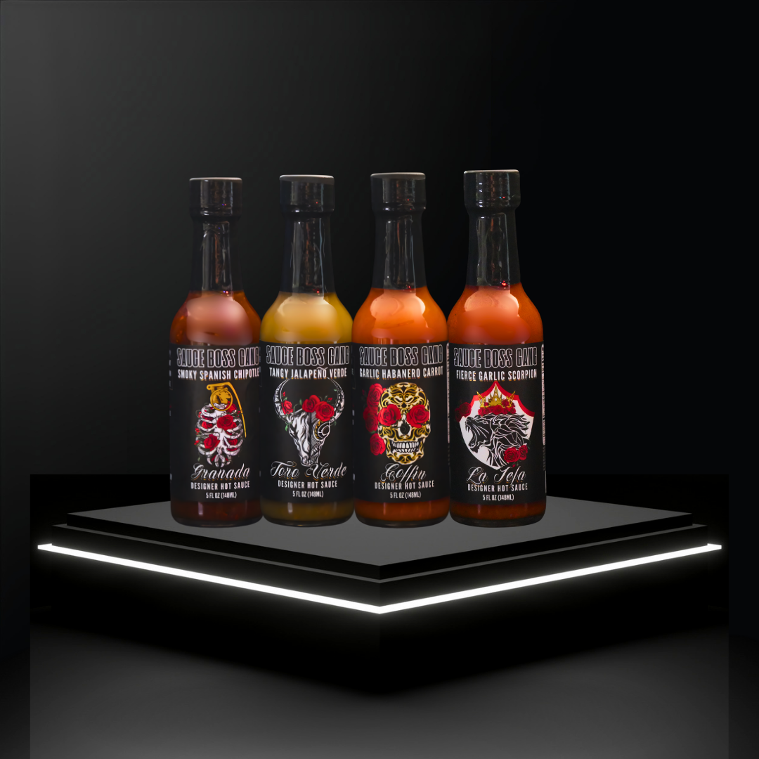 Four bottles of hot sauce with colorful labels on a black platform with white lighting.