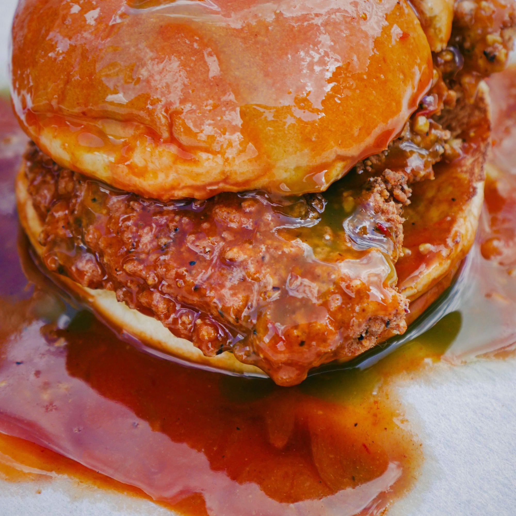 Close-up of a burger with a juicy patty and bun, surrounded by sauce on a white background.