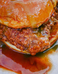 Close-up of a burger with a juicy patty and bun, surrounded by sauce on a white background.