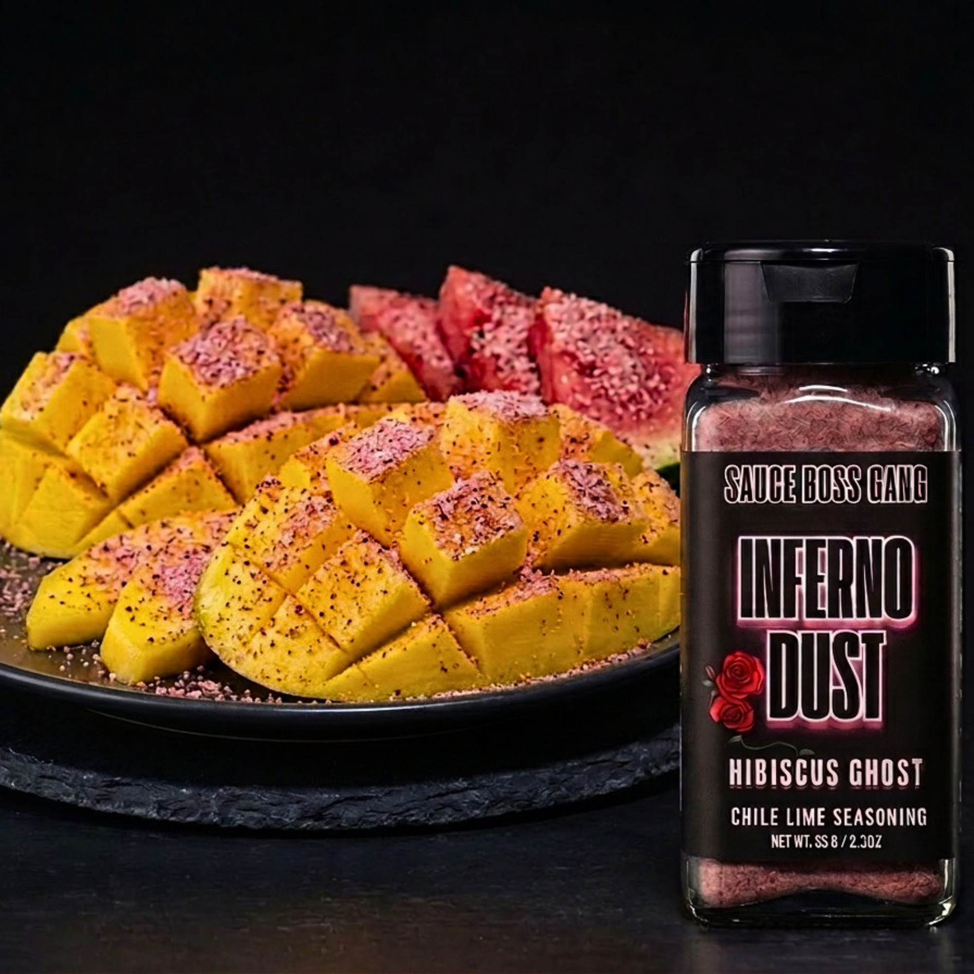 Sauce bottle labeled 'Inferno Dust' next to a plate of sliced yellow and red fruit on a dark background
