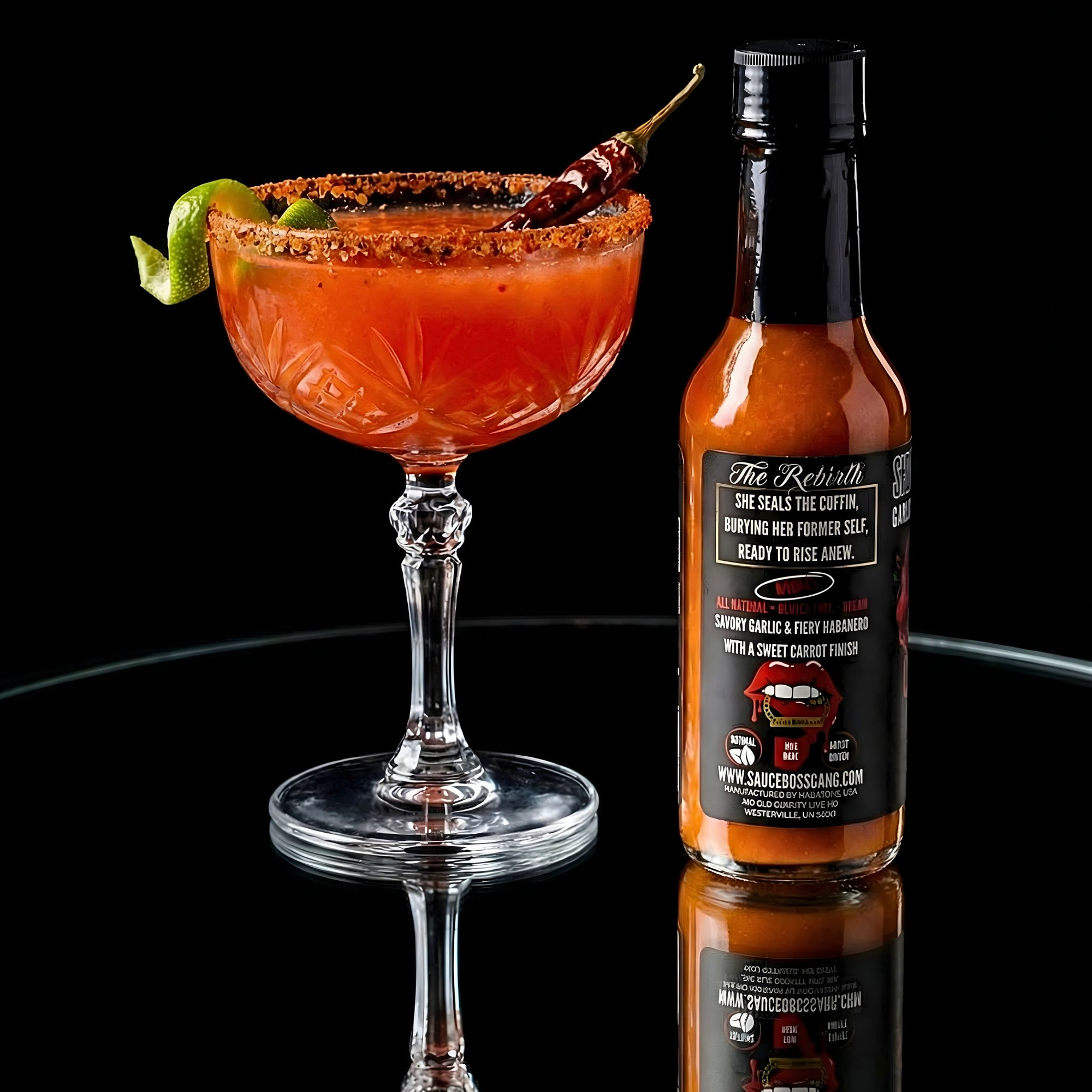 Bottle of hot sauce next to a cocktail with garnishes on a reflective surface