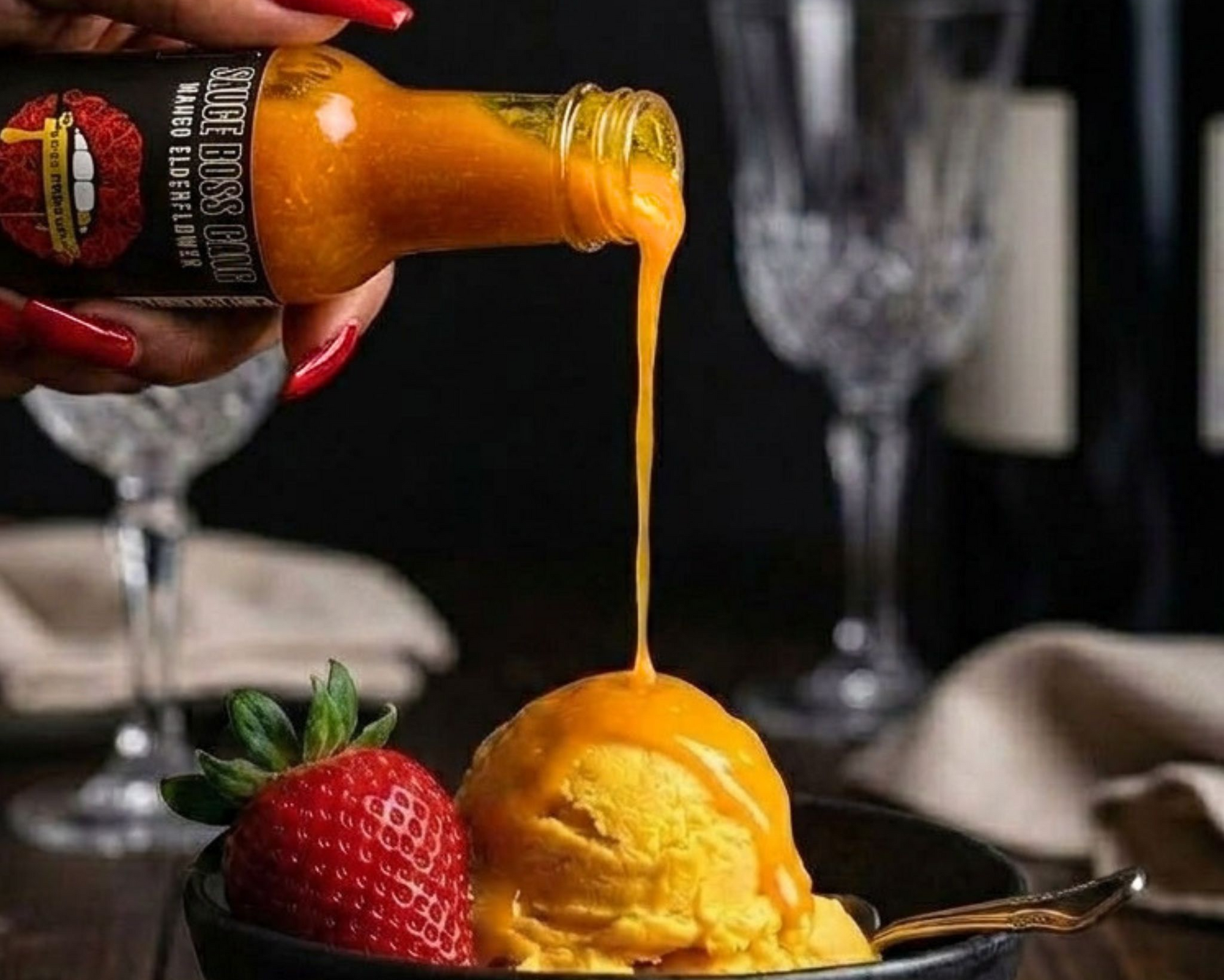 Hot sauce being poured onto a scoop of ice cream with a strawberry on a table setting.